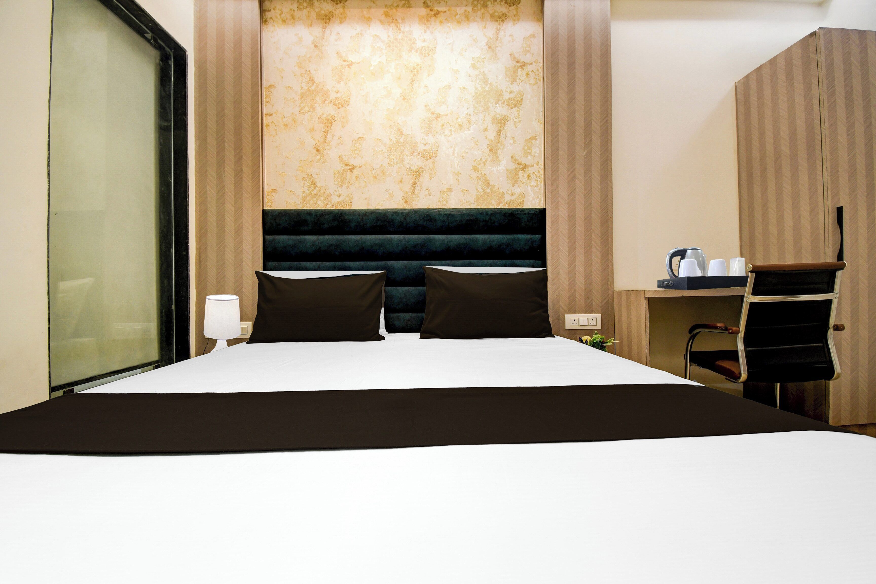 A hotel room with a bed, two pillows, a desk with a chair, a lamp, and a coffee maker.