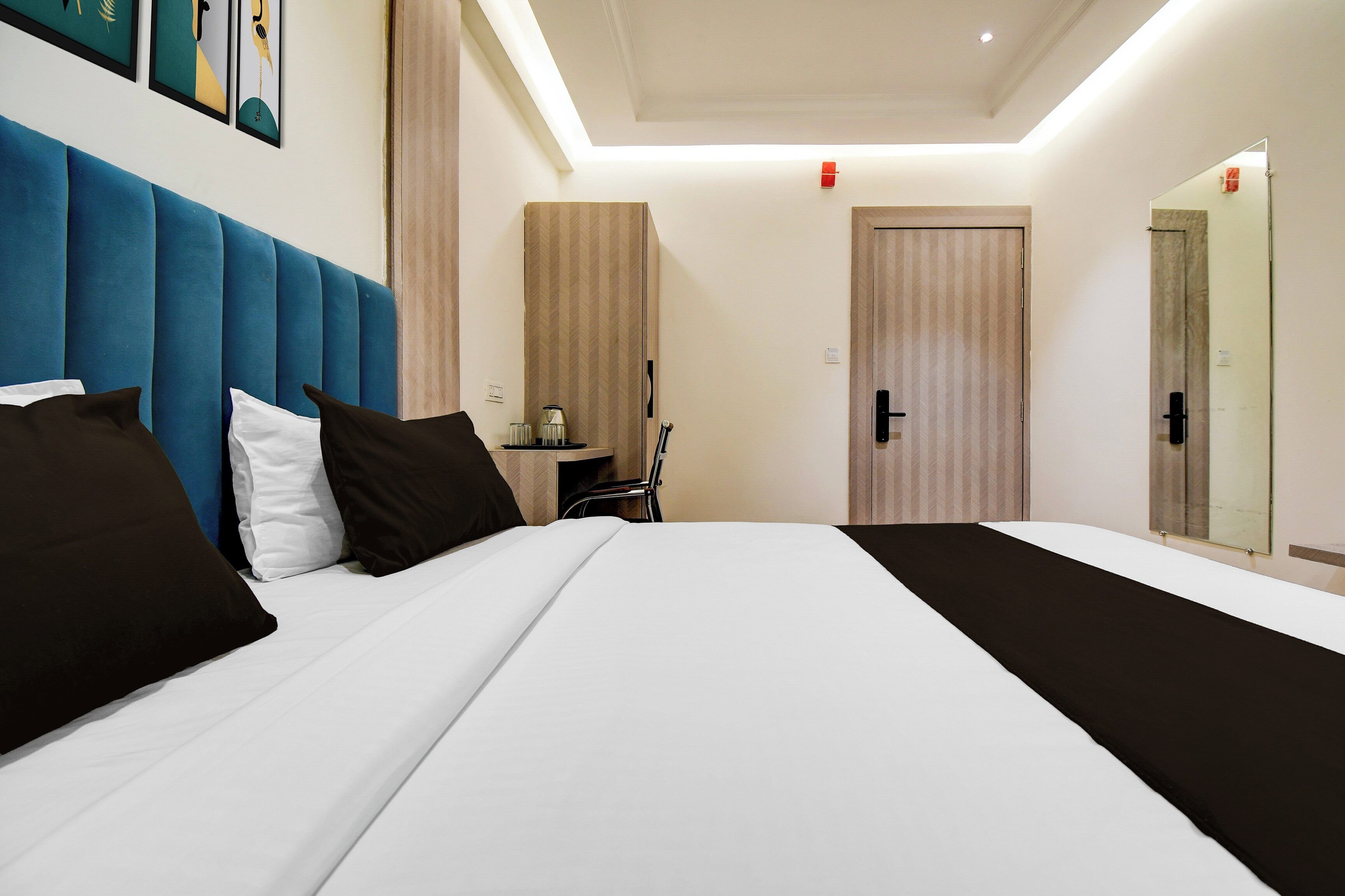 A hotel room with a large bed, a blue headboard, a bedside table with a lamp, and a mirror.
