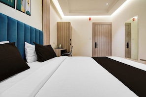 A hotel room with a large bed, a blue headboard, a bedside table with a lamp, and a mirror. - Townhouse Bairhana Road Prayagraj (Prayagraj)