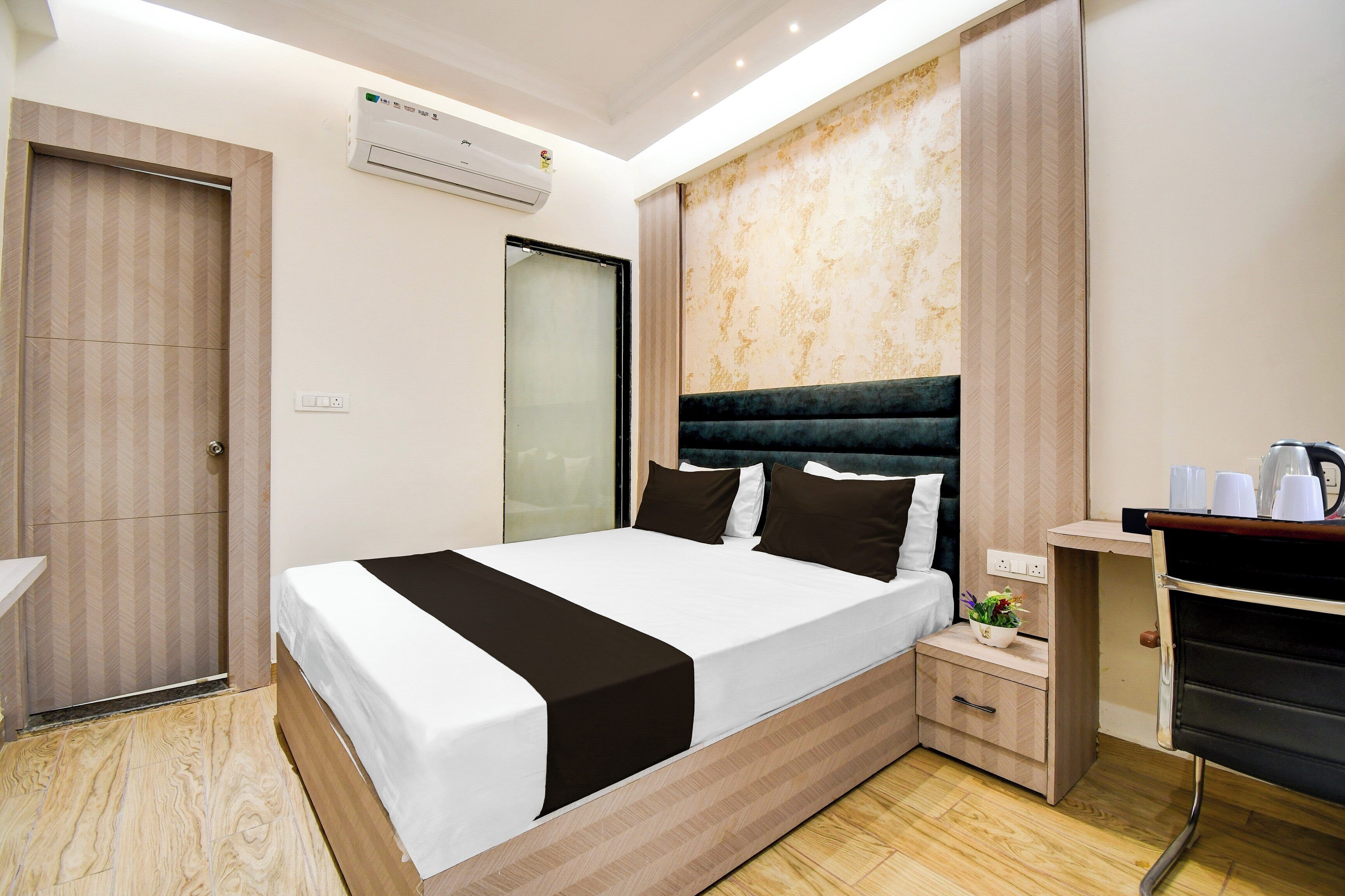 Quarto de hotel moderno com uma cama grande, uma mesinha de cabeceira, uma prateleira embutida e um aparelho de ar condicionado.
