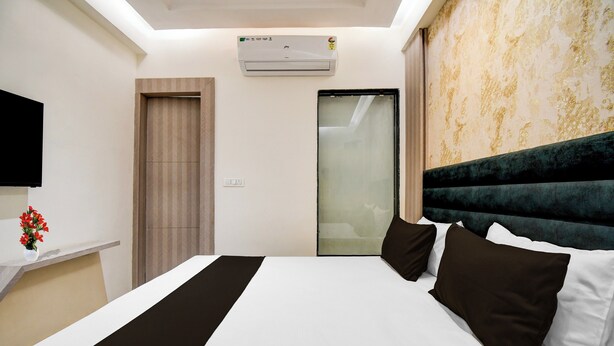 A hotel room with a bed, a flat-screen TV, an air conditioning unit, a wardrobe, and a mirror. - Townhouse Bairhana Road Prayagraj (Prayagraj)