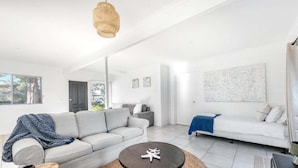 A modern living room with a grey sofa, a round coffee table, and a white couch. - Beach Street Bungalow (Vincentia)