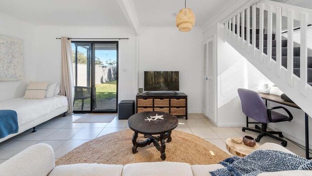 A modern living room with a sofa, a coffee table, a TV, and a staircase. - Beach Street Bungalow (Vincentia)