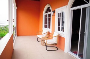 A balcony with two wicker chairs, a white door, and a window with a white frame.