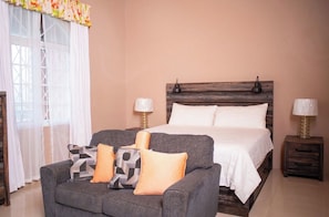 Un dormitorio con cama, mesitas de noche, un sofá y una ventana con cortinas.