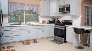 A kitchen with white cabinets, a microwave, a stove, and a coffee maker. -  Entire townhouse in Montego Bay, Jamaica (Montego Bay)