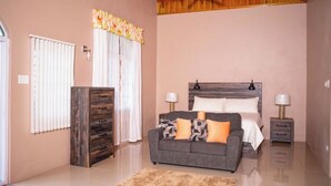 A bedroom with a bed, a sofa, a dresser, a ceiling fan, and a window with curtains. -  Entire townhouse in Montego Bay, Jamaica (Montego Bay)