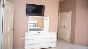 A bedroom with a bed, a dresser, a television mounted above the bed, and two doors. -  Entire townhouse in Montego Bay, Jamaica (Montego Bay)