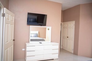 Una camera da letto con un letto, una cassettiera, una televisione montata sopra il letto e due porte.