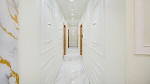 A hallway with white walls, marble flooring, and doors on both sides. - Townhouse Oak Prayagraj Allahabad (Prayagraj)