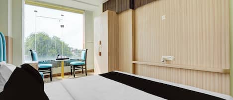 A hotel room with a bed, a small table, two chairs, a window with a view, and a wall with a wooden panel design.