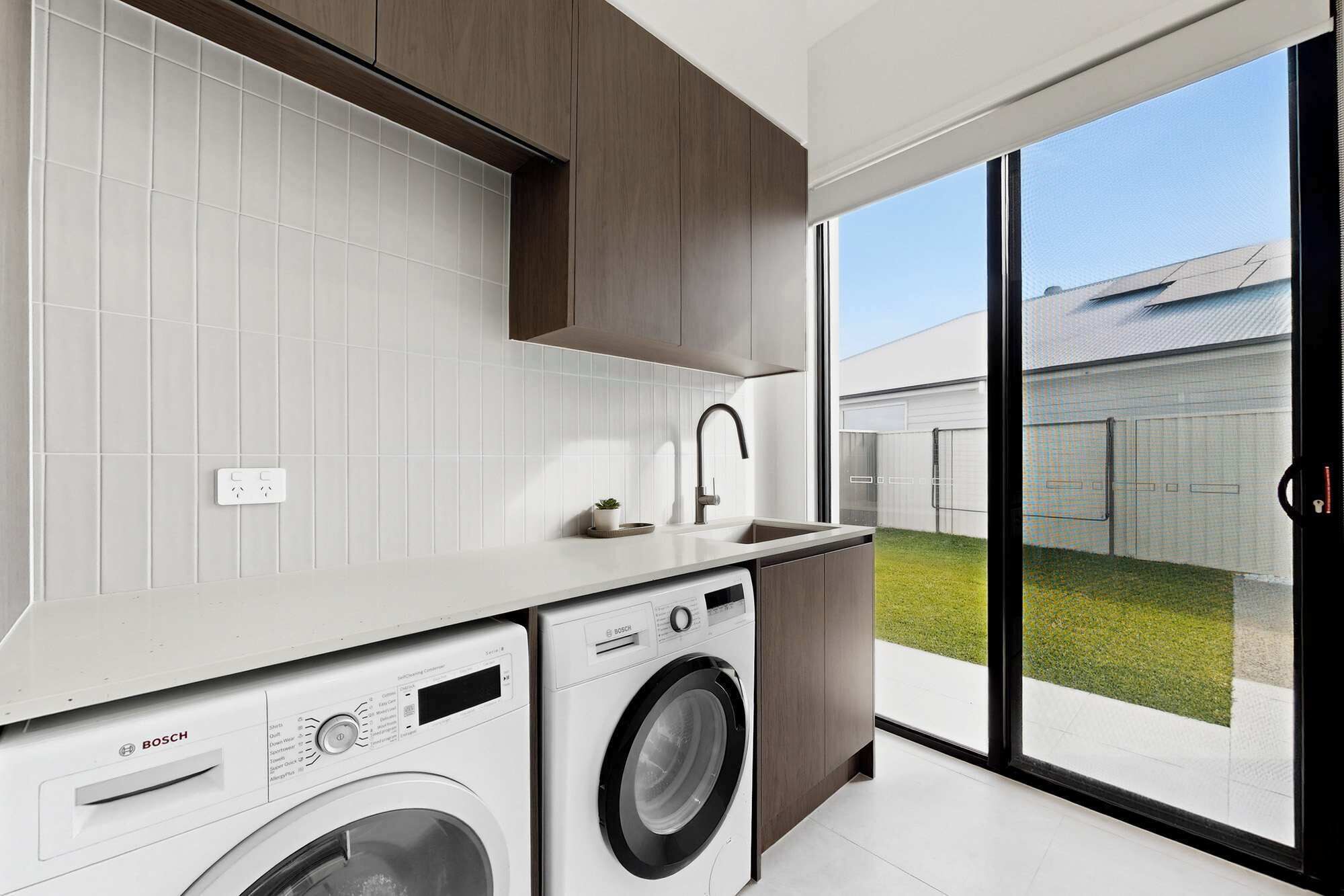 Une cuisine moderne équipée d’un lave-linge, d’un évier et d’une grande porte-fenêtre coulissante donnant sur un jardin.