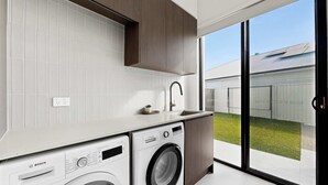 Eine moderne Küche mit Waschmaschine, Spüle und einem großen Schiebeglastür, die in einen Garten führt.