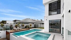 Ein modernes Haus mit Swimmingpool, einer Terrasse und Loungemöbeln sowie einem großen Fenster.