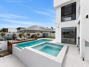A modern house with a swimming pool, a patio with lounge chairs, and a large window. - Luxe Harbour Breeze at Newport (Newport)