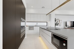 A modern kitchen with a built-in oven, a sink, and a television. - Luxe Harbour Breeze at Newport (Newport)
