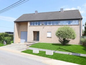 Ein zweistöckiges Haus mit Ziegeldach, einem kleinen Vorgarten mit Gras und einem Baum sowie einer Auffahrt zum Eingang.