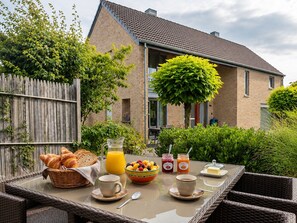 Ein draußen aufgebautes Frühstücksbuffet mit Croissants, Früchten, Saft und Kaffee auf einem Korbtisch.