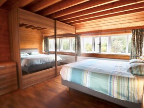 Une chambre dans un chalet en bois, avec deux lits, de grandes fenêtres et une vue sur l’extérieur.