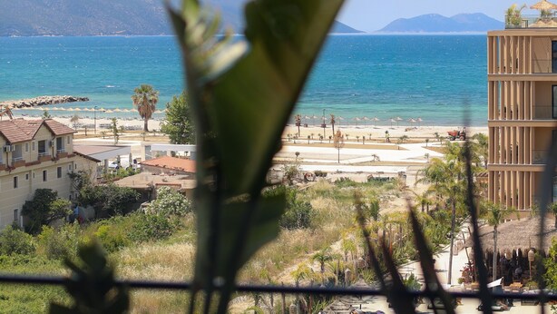 A coastal view with a beach, a mountain range, and a building with balconies overlooking the sea. - Majestic View Apartment Palm (Orikum)