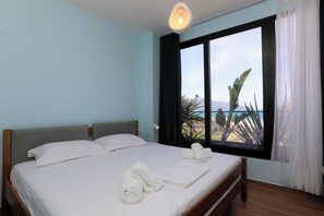 A hotel room with a bed, a window with curtains, and a view of the beach. - Majestic View Apartment Palm (Orikum)