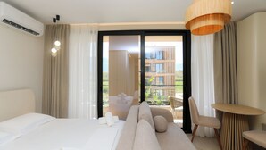 Habitación de hotel con cama, sofá, mesa de comedor y vista a un edificio a través del ventanal.