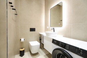 Ein modernes Badezimmer mit Toilette, Waschbecken, Spiegel und Waschmaschine.