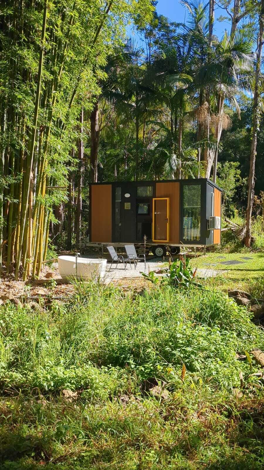 A modern, compact cabin with a wooden exterior, a door, and a small porch area with a chair.