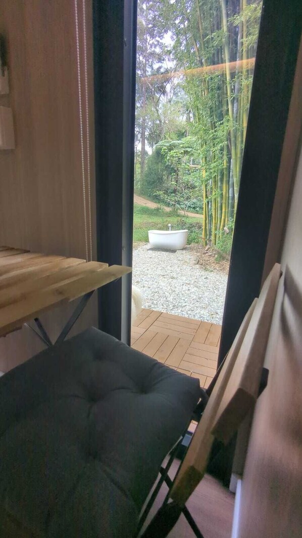 A room with a view of a garden, a white bathtub, and a wooden table.