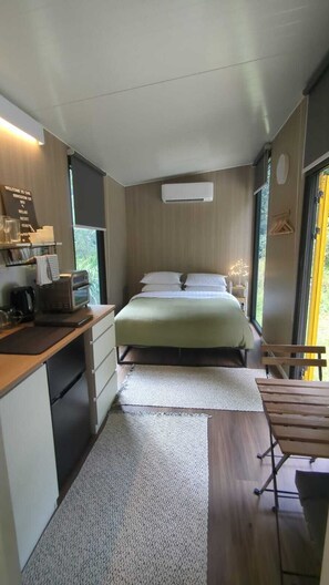 Habitación de hotel pequeña con cama, escritorio, silla y una kitchenette.