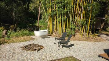 A garden area with a fire pit, two chairs, and a large white tub.