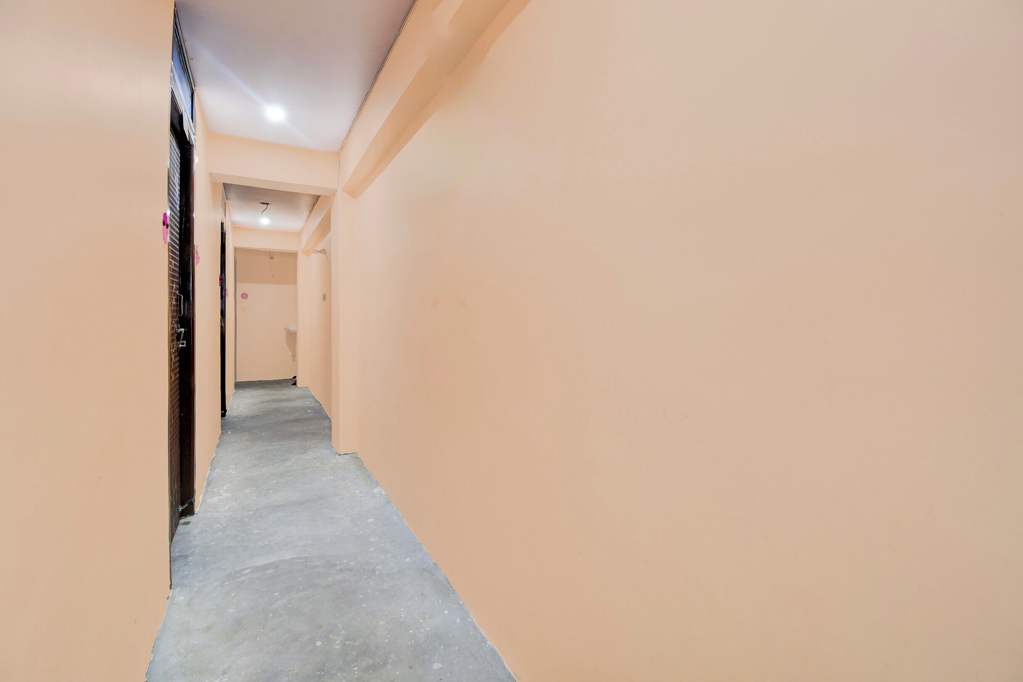 A corridor with a concrete floor and beige walls, leading to a room with a door at the end.