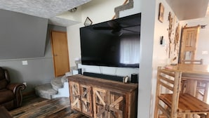 A living room with a large flat-screen TV, wooden furniture, and a stone fireplace.