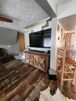 A living room with a large flat-screen TV, wooden furniture, and a stone fireplace. - Upper Main Cabin is a 4-bedroom cabin in tranquil Loon Lake (Loon Lake)