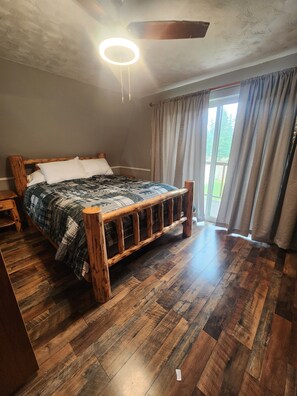 A bedroom with a wooden bed, a ceiling fan, and a view through a window with curtains. - Upper Main Cabin is a 4-bedroom cabin in tranquil Loon Lake (Loon Lake)