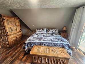 A bedroom with a sloped ceiling, a wooden bed with a quilt, a nightstand, and a wooden cabinet.