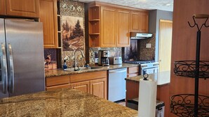 A kitchen with granite countertops, wooden cabinets, a stainless steel refrigerator, a coffee maker, and a toaster.