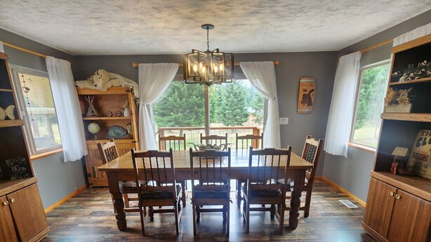 Un espace repas avec une table et des chaises en bois, un lustre et une vue sur l’extérieur grâce à de grandes fenêtres.