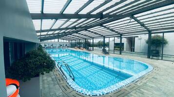 An indoor swimming pool with clear blue water, surrounded by lounge chairs and potted plants.