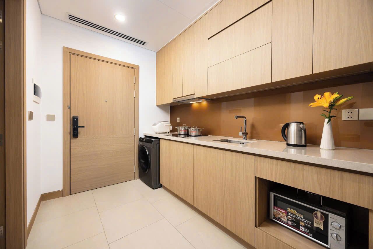A modern kitchen with wooden cabinets, a built-in washing machine, a sink, and a microwave.