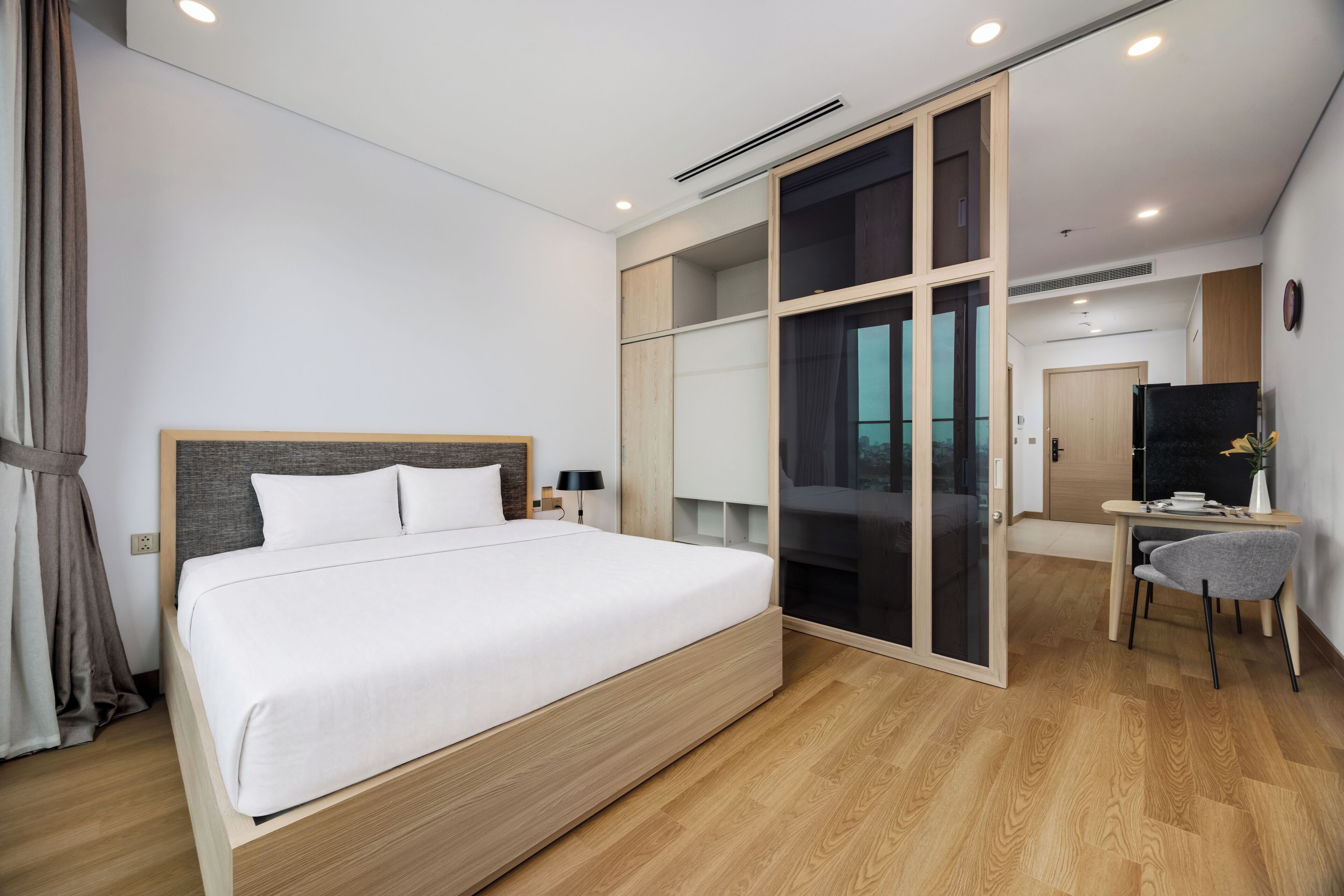 Una habitación de hotel moderna con una cama grande, un escritorio y un ventanal corredero que da a un balcón.