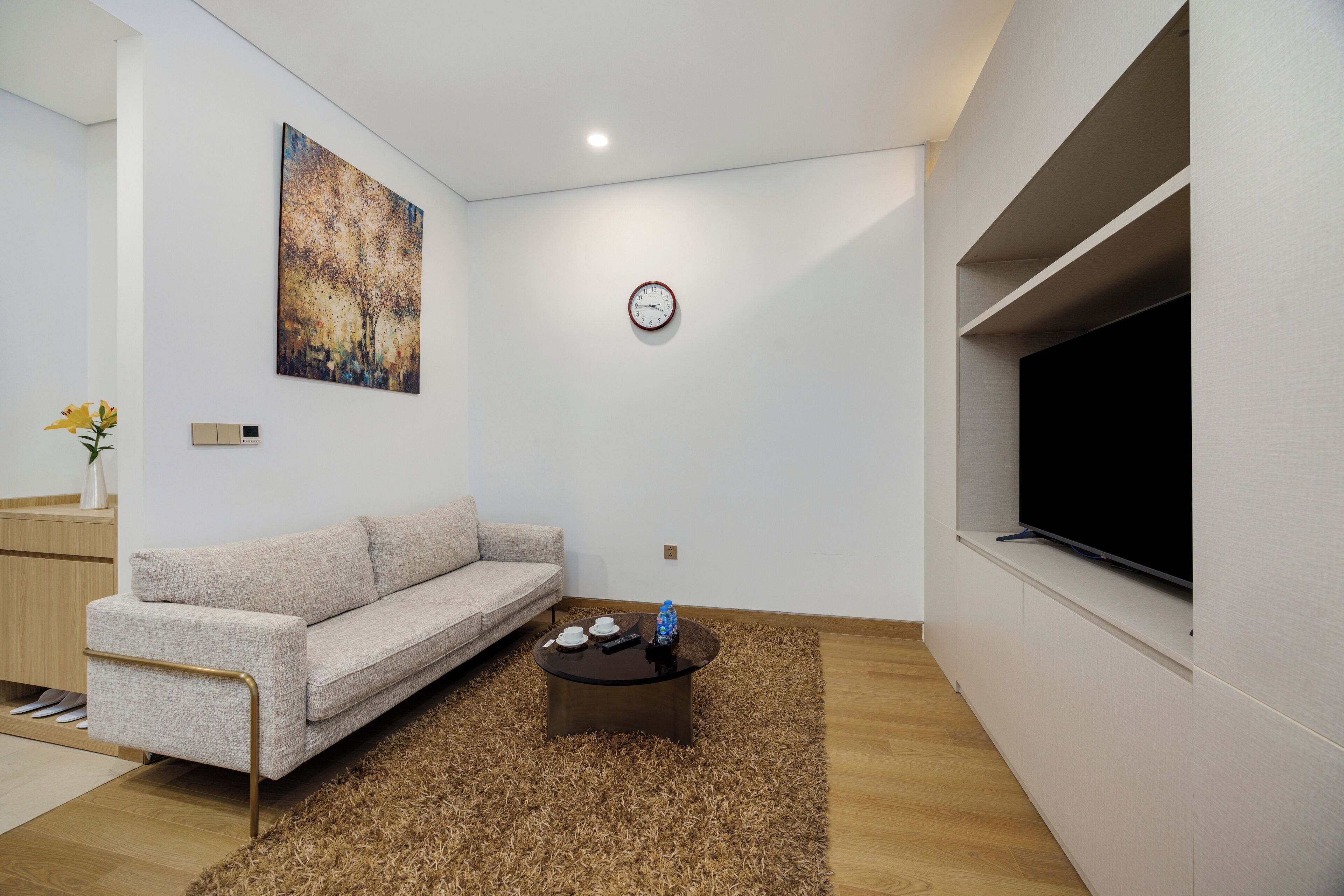 Een moderne woonkamer met een bank, een salontafel, een schilderij, een klok en een televisie.