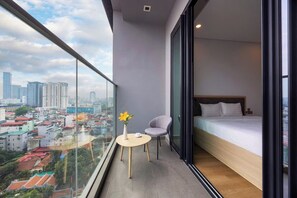 A modern bedroom with a large window, a bed, a small table with a vase, and a chair. - Lancaster Apartment (Hanoi)