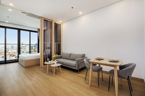 Una sala moderna con un sofá, una mesa de comedor con sillas, una mesita redonda con un florero y un ventanal con vista a la ciudad.