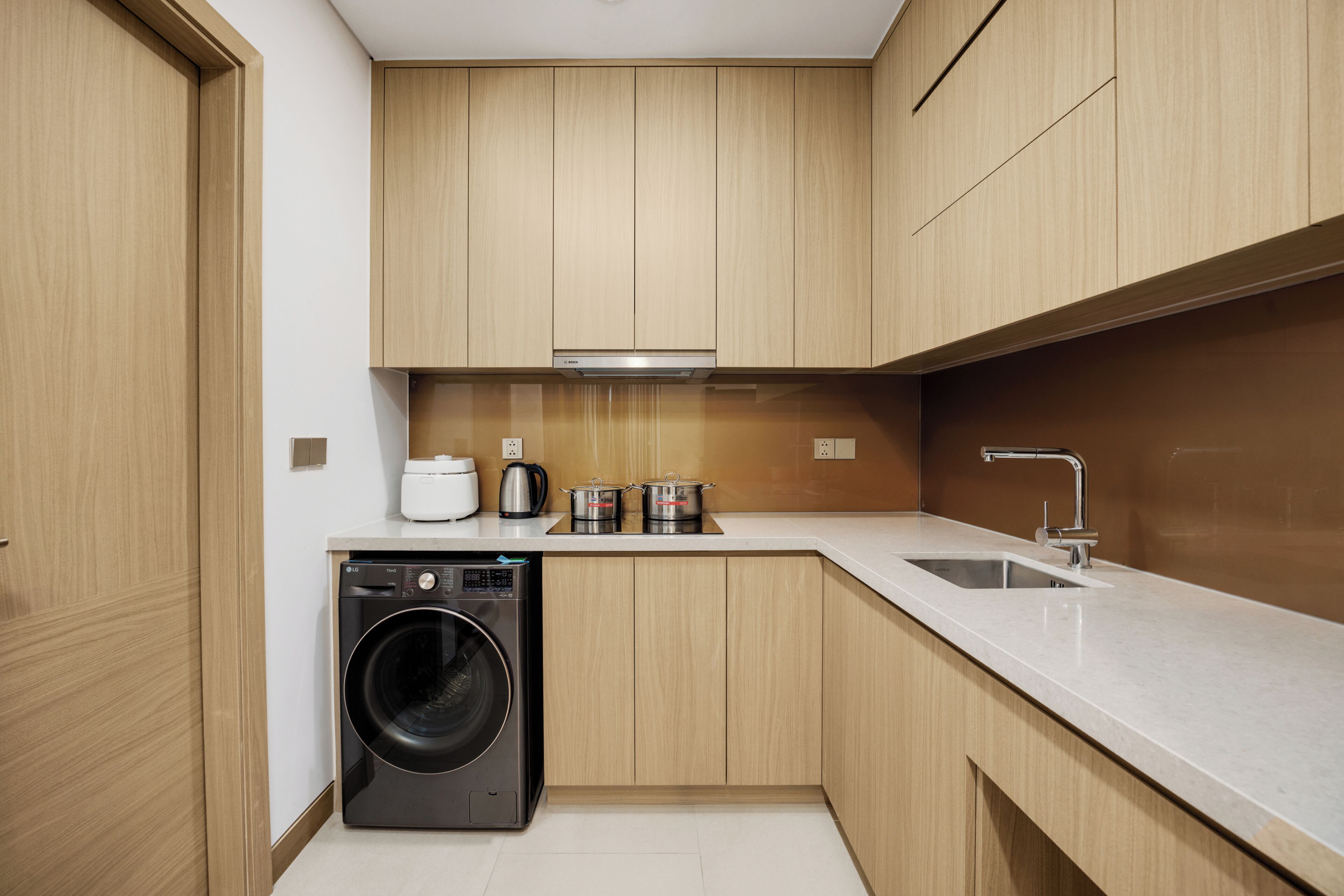 A compact kitchen with wooden cabinets, a built-in washing machine, a sink, and a stove.