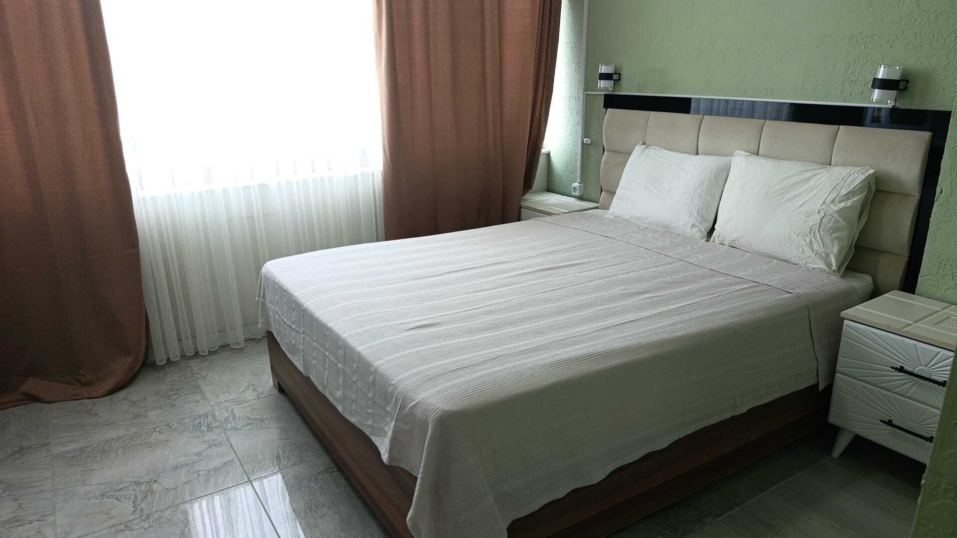 A hotel room with a large bed, a nightstand, a lamp, and a window with curtains.
