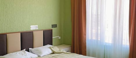 A hotel room with a large bed, green walls, a window with curtains, and a white ceiling.