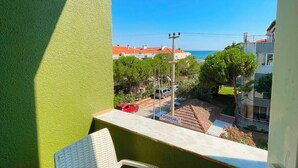 A balcony with a white chair, a green wall, and a clear view of the sea and buildings in the distance. - Empati Otel (Ayvalık)
