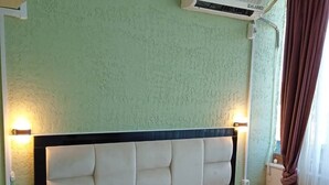 A bedroom with a bed, bedside tables, a nightstand, a wall-mounted air conditioner, and a window with curtains. - Empati Otel  (Ayvalık)