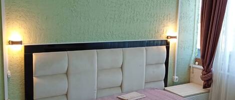A bedroom with a bed, bedside tables, a nightstand, a wall-mounted air conditioner, and a window with curtains.